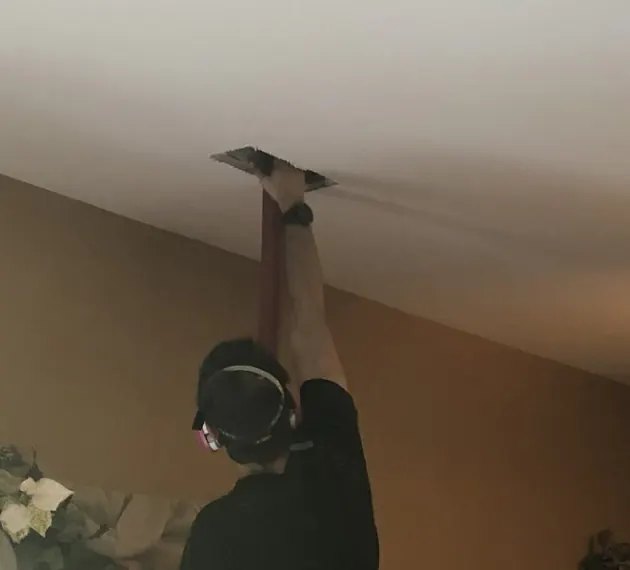 A Bactronix technician on a ladder in a customer's living room, working a hose into a ceiling register